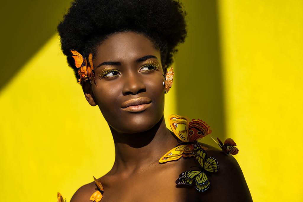 Χαμογελαστή όμορφη αφρικανική Αμερικάνα γυναίκα με πεταλούδες στο κίτρινο - Φωτογραφία, εικόνα