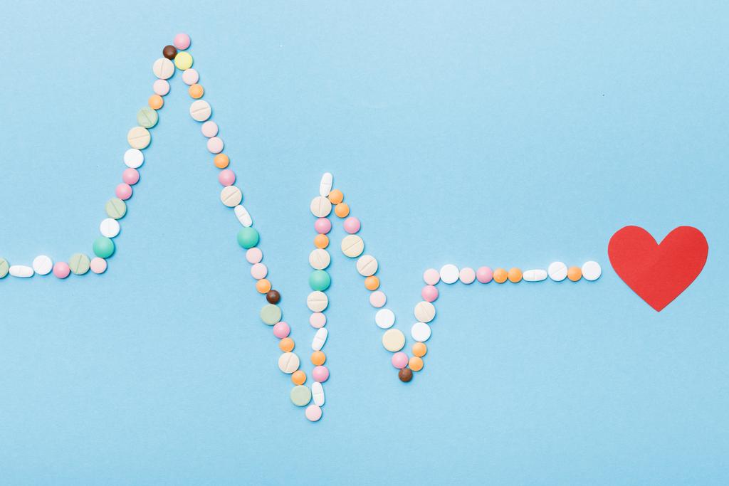 Pose plate avec des pilules colorées et coeur en papier sur bleu
 - Photo, image