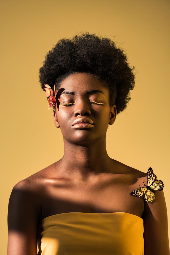 Femme afro-américaine détendue avec des papillons aux yeux fermés isolés sur brun
 - Photo, image