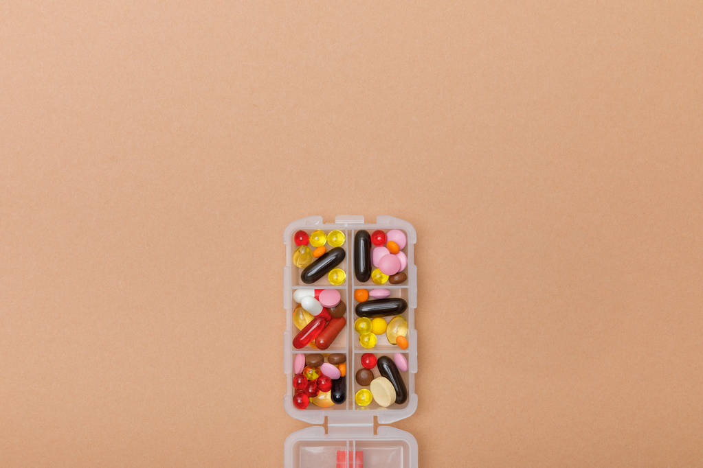 Widok z góry pojemnika z kolorowymi tabletkami na brązowej powierzchni - Zdjęcie, obraz