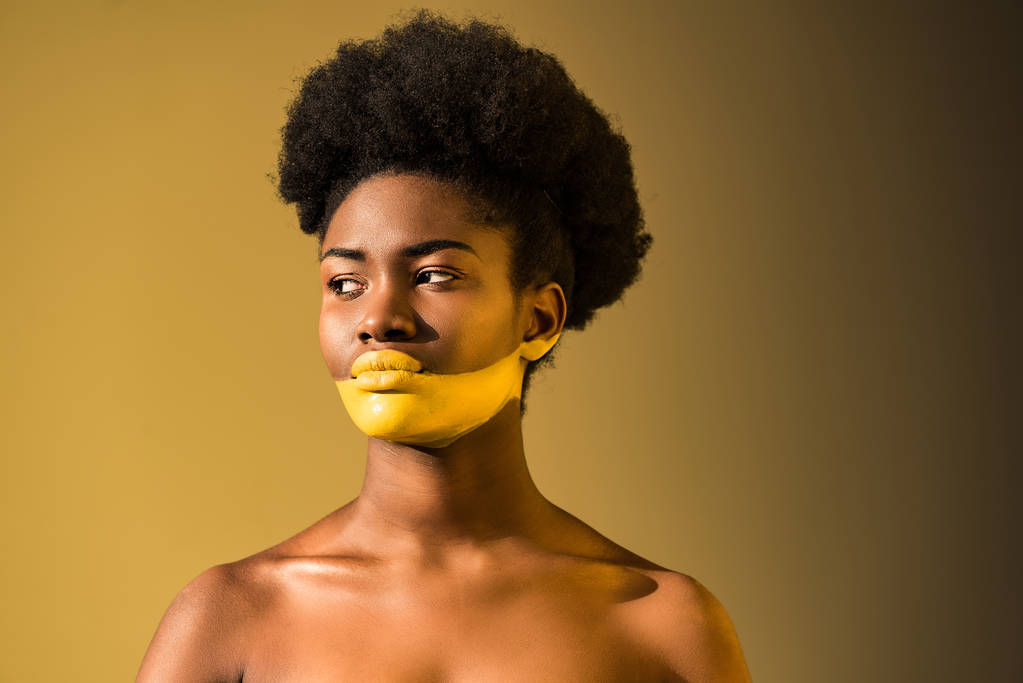 Mujer afroamericana seria con el arte del cuerpo amarillo en marrón
 - Foto, imagen