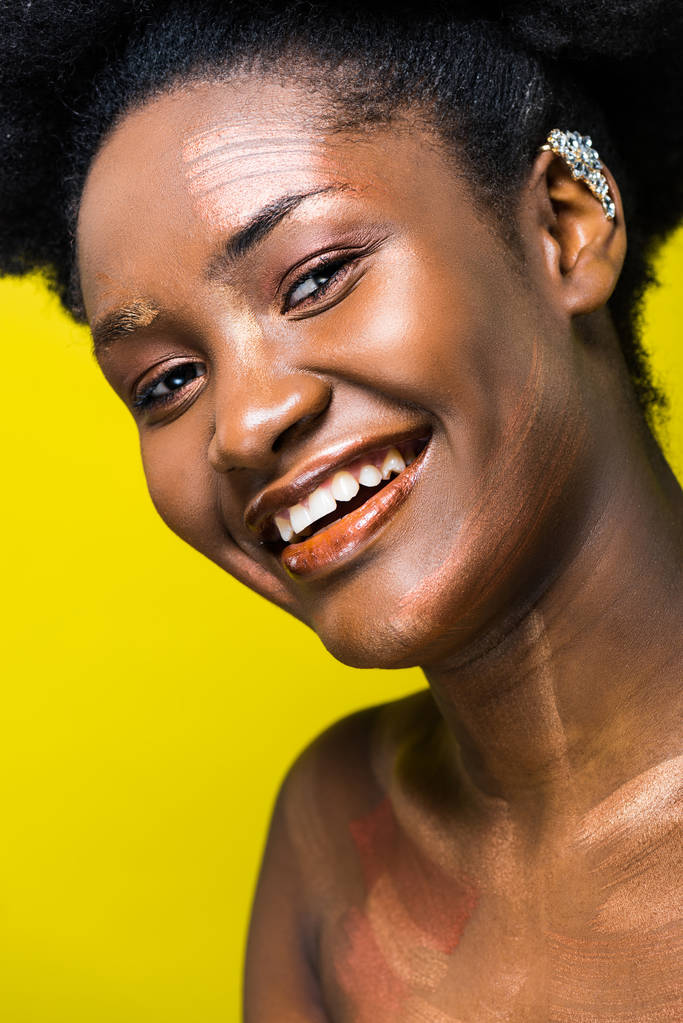 Χαμογελαστή Αφρικανική Αμερικανίδα γυναίκα στο αυτί κοιτάζει την κάμερα απομονώνεται σε κίτρινο - Φωτογραφία, εικόνα