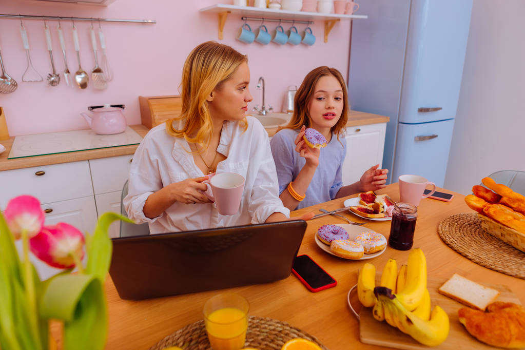 Meisje eten teveel snoep terwijl oudere zus online werken - Foto, afbeelding