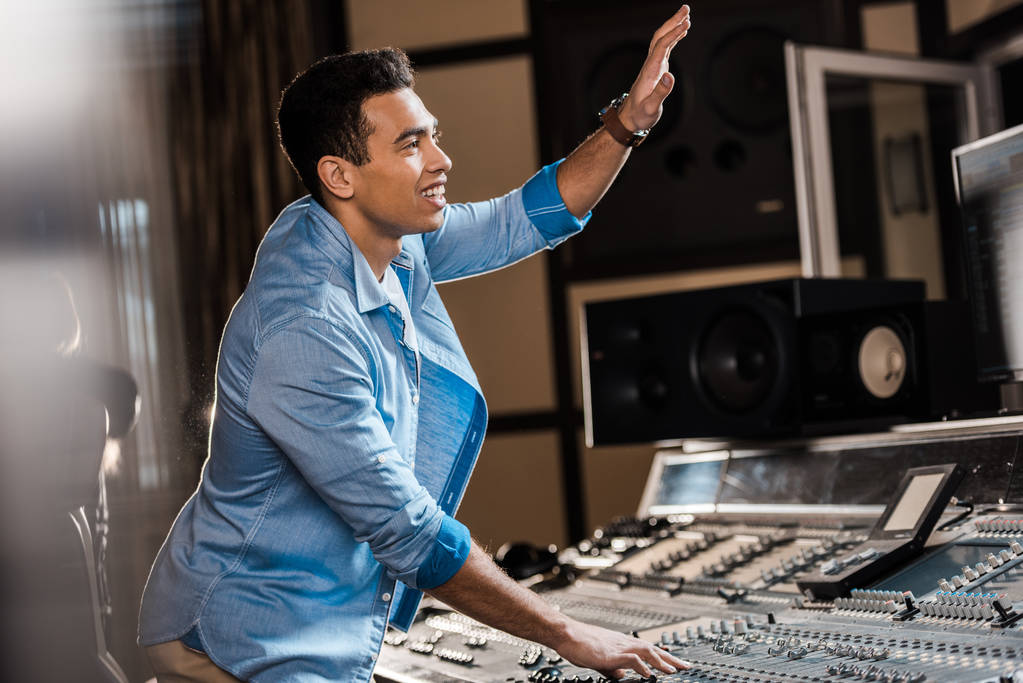 избирательный фокус улыбающегося продюсера смешанного расового звука, жестикулирующего во время работы в студии звукозаписи
 - Фото, изображение