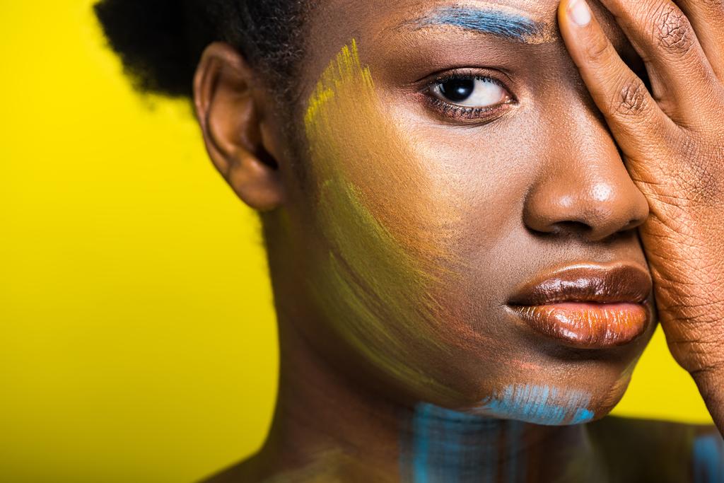 Mulher americana africana Pensiva com corpo arte tocando rosto com a mão no amarelo
 - Foto, Imagem