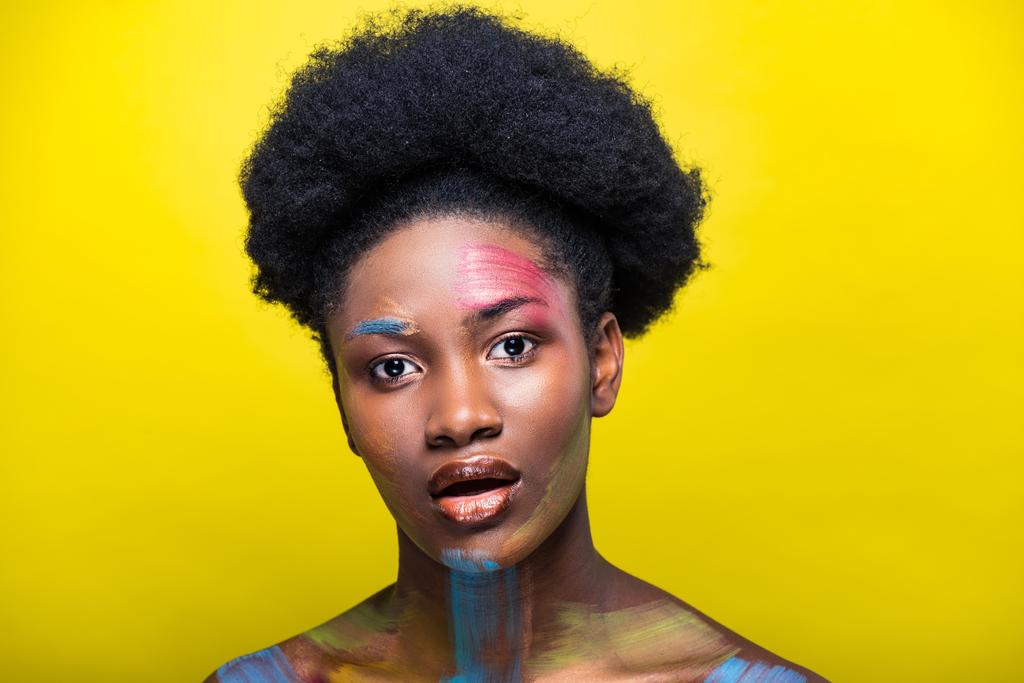Удивлённая африканская американка с ярким макияжем смотрит в камеру на жёлтом
 - Фото, изображение