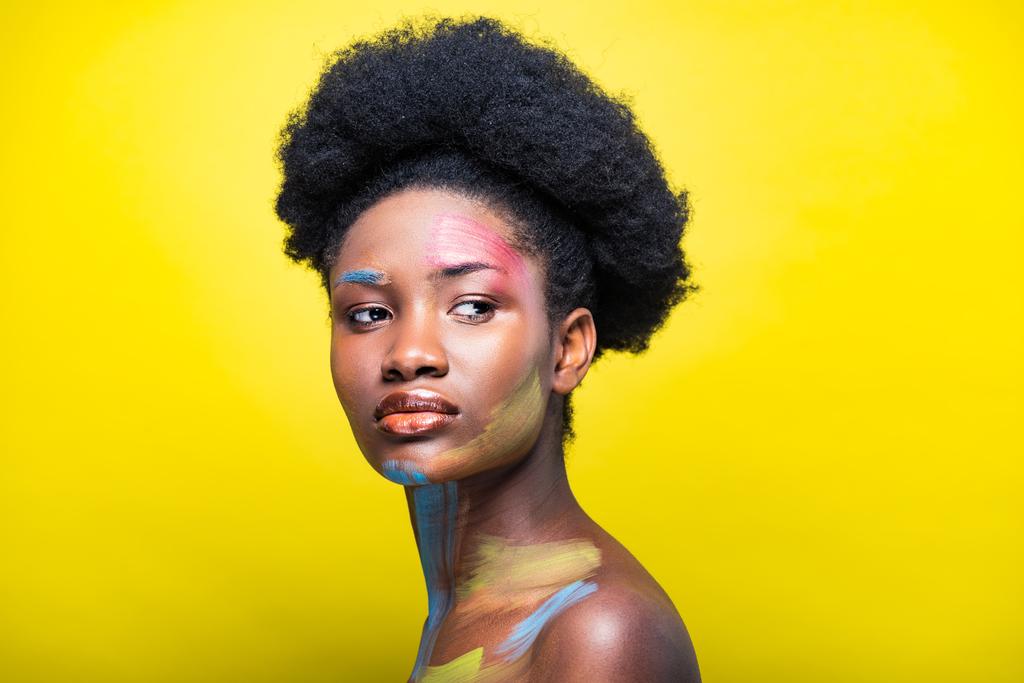 Σκεπτική αφρικανική Αμερικανίδα γυναίκα με πολύχρωμη τέχνη του σώματος στο κίτρινο - Φωτογραφία, εικόνα