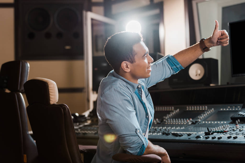 producteur sonore mixte souriant montrant pouce levé tout en travaillant dans un studio d'enregistrement
 - Photo, image