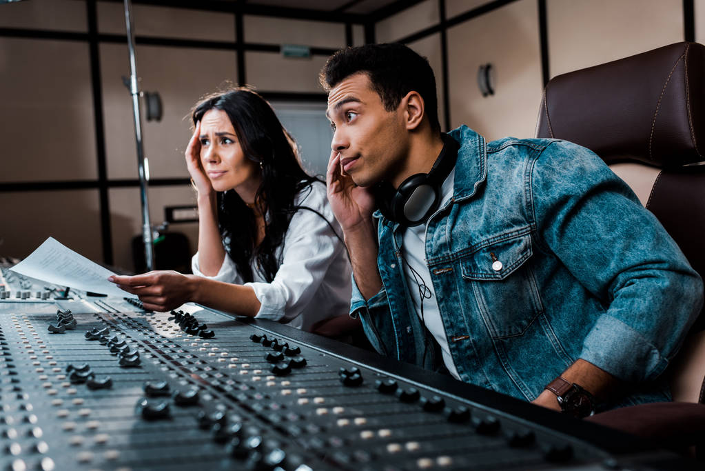 two thoughtful sound producers working at mixing console in recording studio - Photo, Image