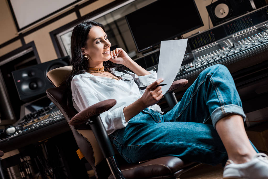 hermoso productor de sonido sonriente sentado en la silla de la oficina cerca de la consola de mezcla en el estudio de grabación
 - Foto, imagen