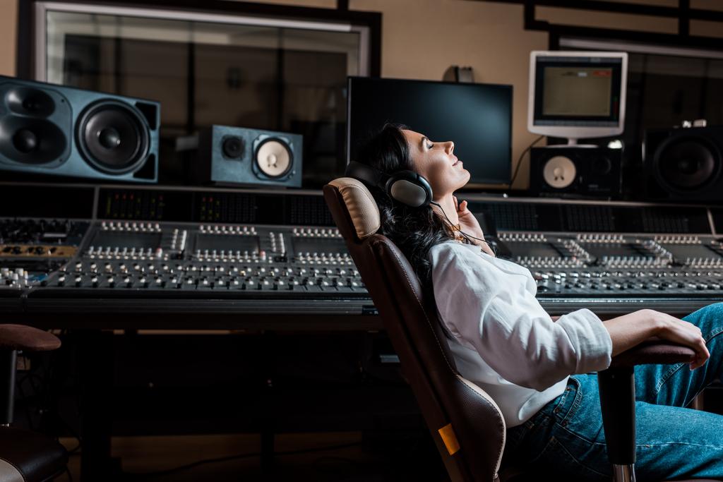 hübscher Soundproduzent, der Musik im Kopfhörer hört, während er im Bürostuhl im Tonstudio sitzt - Foto, Bild