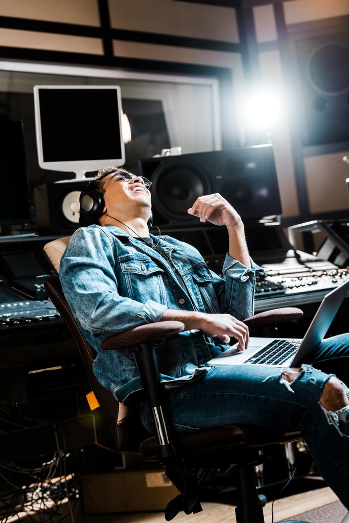 hymyilevä sekamelskan tuottaja kuulokkeissa kuuntelemassa musiikkia valkoinen istuu toimistotuolissa
 - Valokuva, kuva