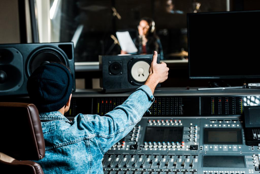 karışık ırk ses yapımcısı seçici odak kayıt stüdyosunda şarkı kadın başparmak kadar gösteren - Fotoğraf, Görsel