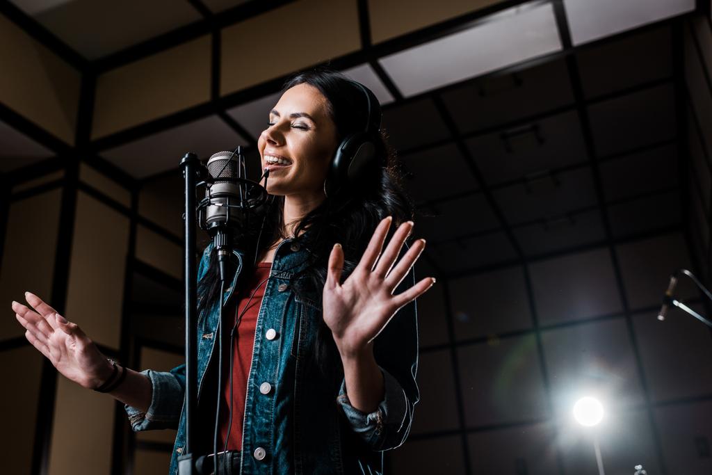 привлекательная вдохновленная женщина поет возле микрофона в студии звукозаписи
 - Фото, изображение