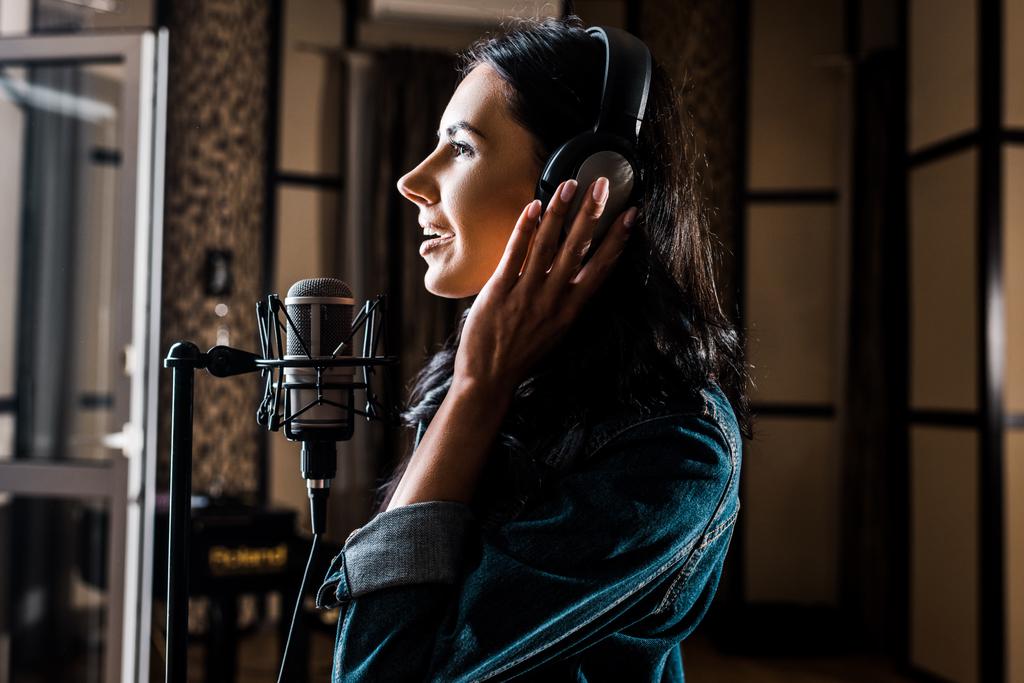 oldalnézetből gyönyörű nő énekelnek a mikrofon közelében stúdióban - Fotó, kép