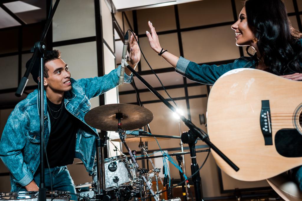 jóvenes músicos multiculturales sonrientes dando cinco en el estudio de grabación
 - Foto, Imagen