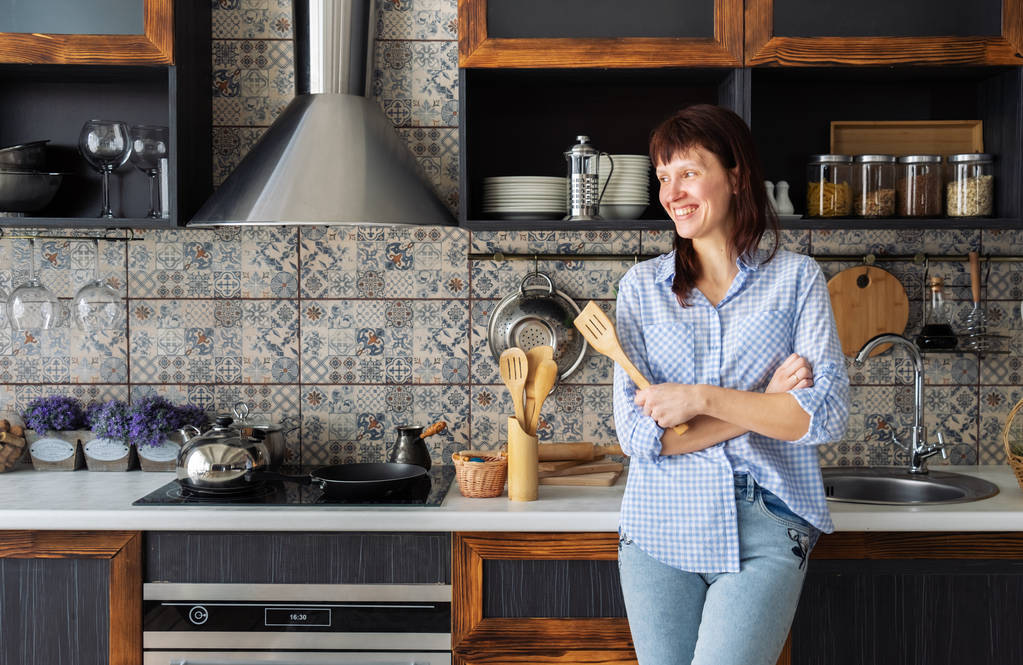 Housewife: young woman with a spatula in her hands smiling in the kitchen. European style interior. - Photo, Image