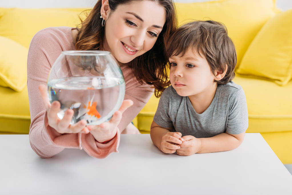 smiling mother holding fish bowl near adorable son at home - Photo, Image