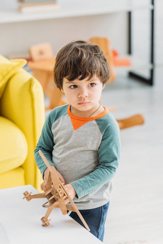 прелестный серьезный ребенок держит деревянный самолет модель дома
 - Фото, изображение