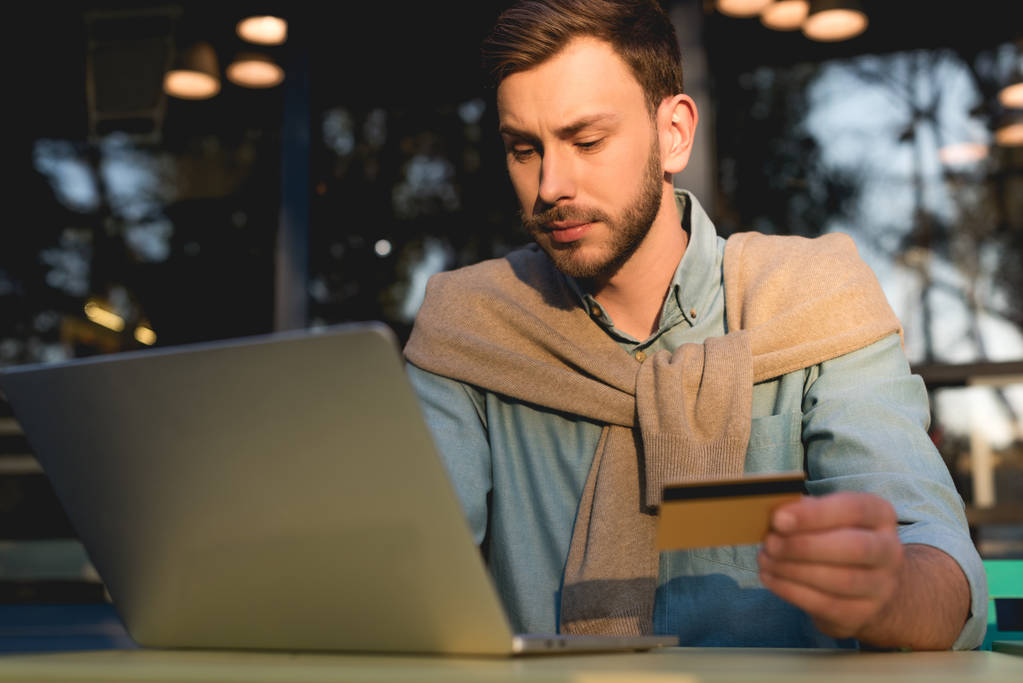 przystojny człowiek trzyma karty kredytowej podczas korzystania z laptopa  - Zdjęcie, obraz