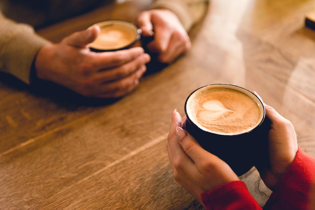 カフェでコーヒーでカップを保持している男性と若い女性のクロップドビュー  - 写真・画像