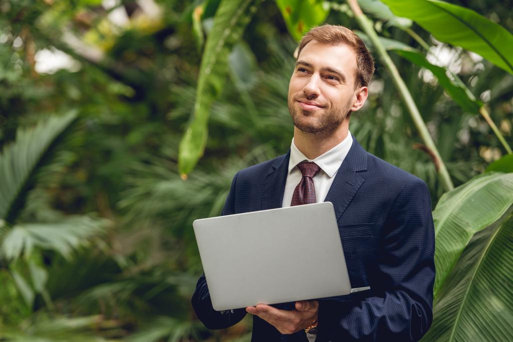 homme d'affaires rêveur souriant en costume et cravate en utilisant un ordinateur portable en orangerie
 - Photo, image