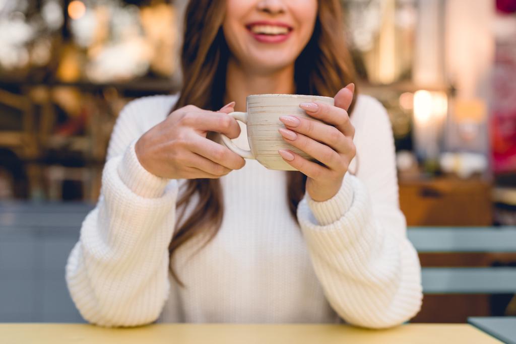περικομμένη θέα της χαρούμενα κορίτσι κρατώντας Κύπελλο με καφέ στο καφέ  - Φωτογραφία, εικόνα