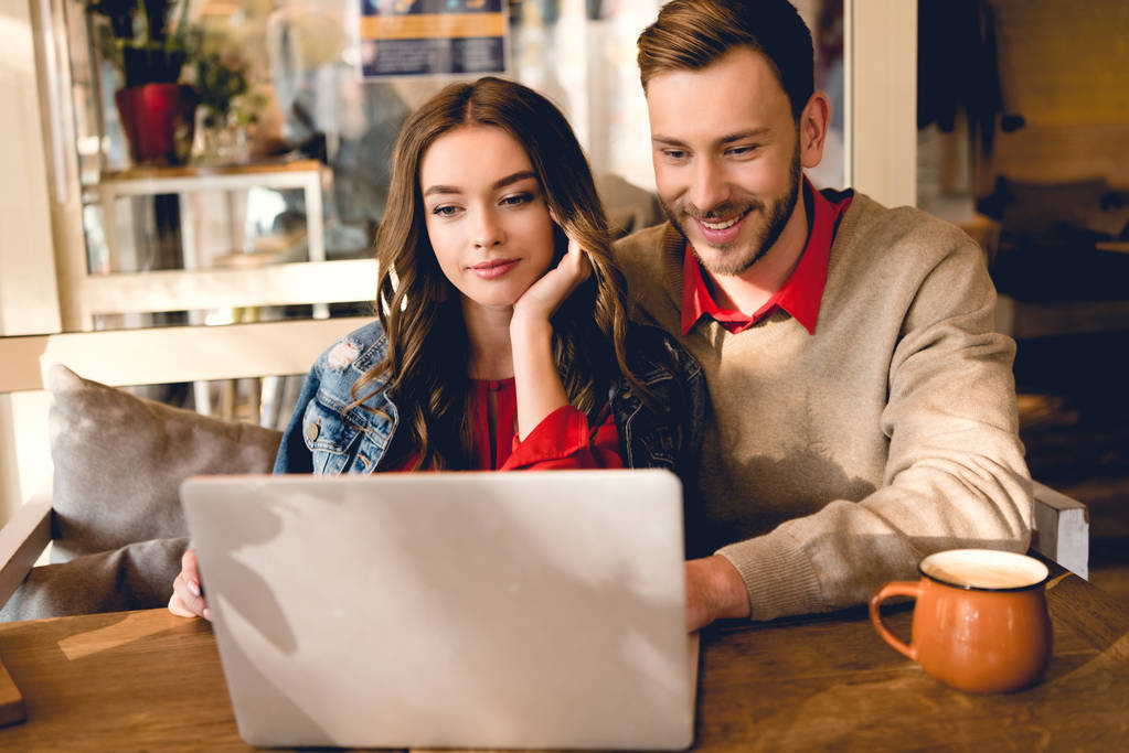 cheerful man and attractive young woman looking at laptop in cafe  - Photo, Image