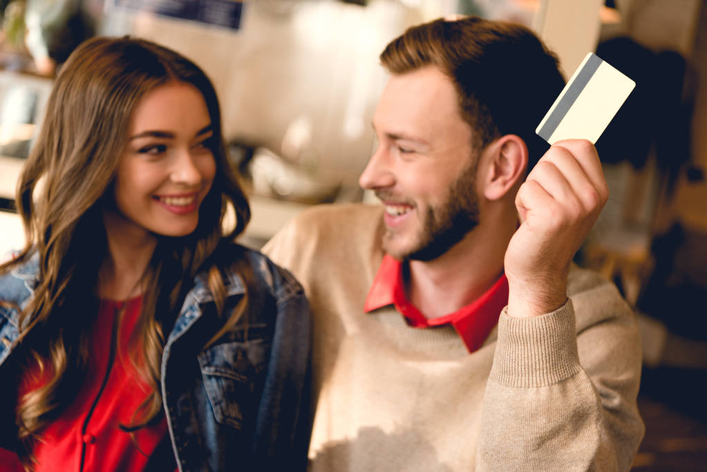 veselý muž držící kreditní kartu a dívat se na šťastnou mladou ženu v kavárně  - Fotografie, Obrázek