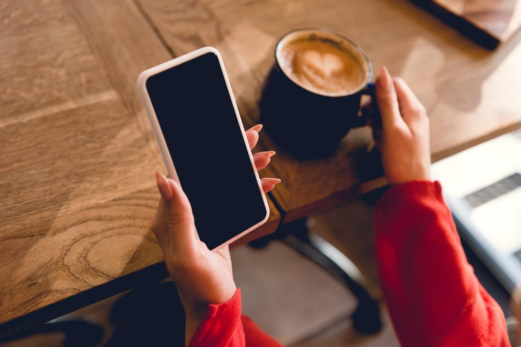 vista recortada de la mujer sosteniendo teléfono inteligente con pantalla en blanco cerca de la taza de café
  - Foto, Imagen