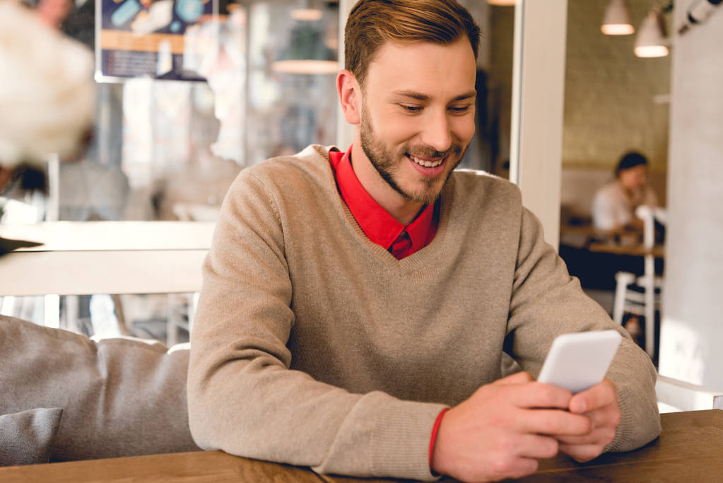 glücklicher bärtiger Mann blickt auf Smartphone und lächelt im Café  - Foto, Bild