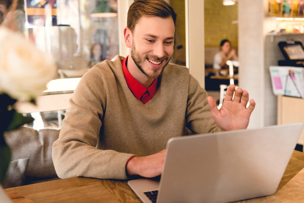 счастливый блоггер машет рукой, имея видео-чат на ноутбуке в кафе
 - Фото, изображение