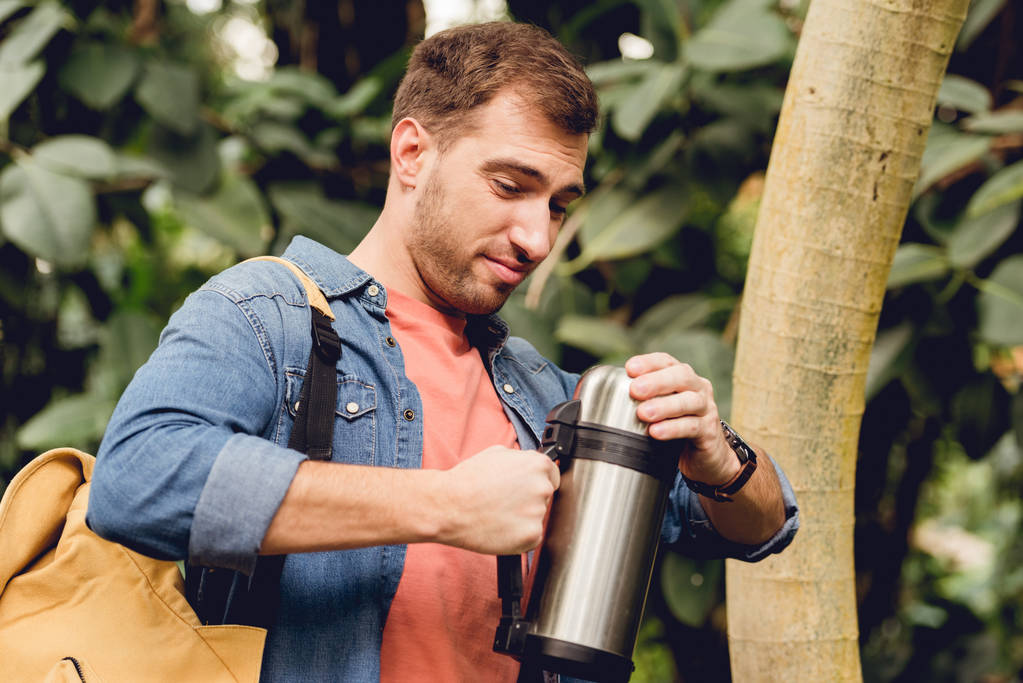 traveler with backpack opening thermos in tropical forest - Photo, Image