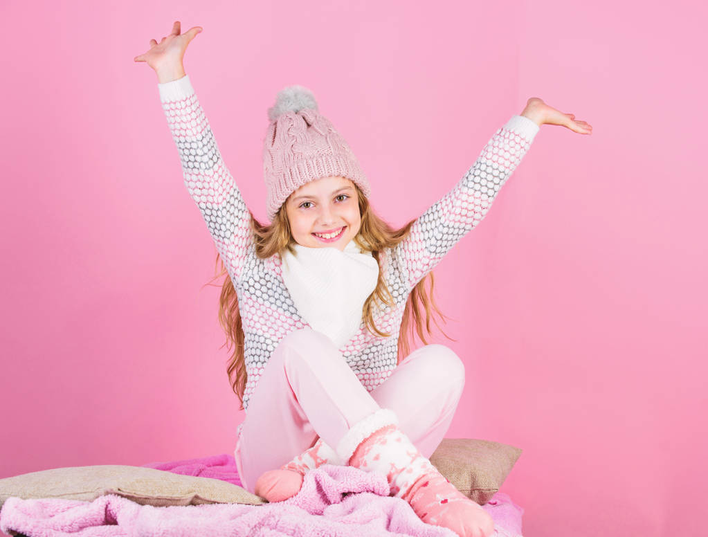 Παιδί κορίτσι φθορά πλεκτό καπέλο χαλαρωτικό ροζ φόντο. Το παιδί μακριά μαλλιά ζεστό μάλλινο καπέλο να απολαύσετε ζεστό. Έννοια ζεστά ρούχα. Ζεστά αξεσουάρ που θα σας κρατήσει άνετα αυτό το χειμώνα. Κρατήσει ζεστό και άνετα - Φωτογραφία, εικόνα