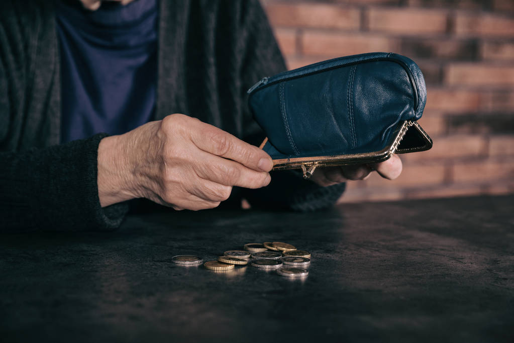 Бедная зрелая женщина выливает монеты из бумажника за стол, крупным планом
 - Фото, изображение