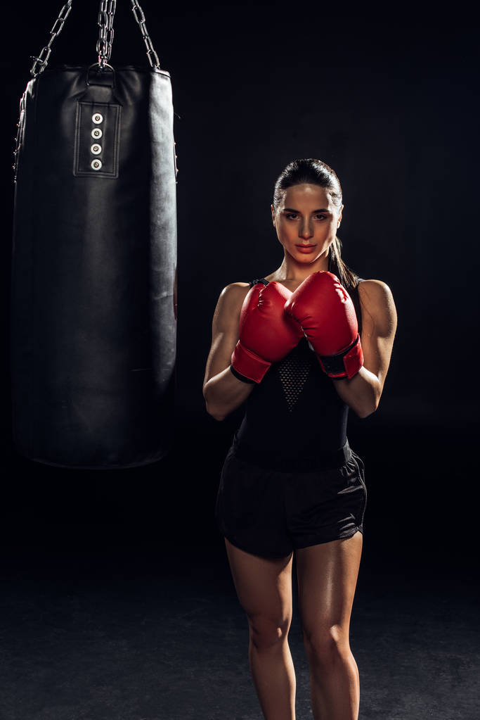 Edessä näkymä nyrkkeilijä punainen nyrkkeily käsineet seisoo lähellä nyrkkeilysäkki musta
 - Valokuva, kuva