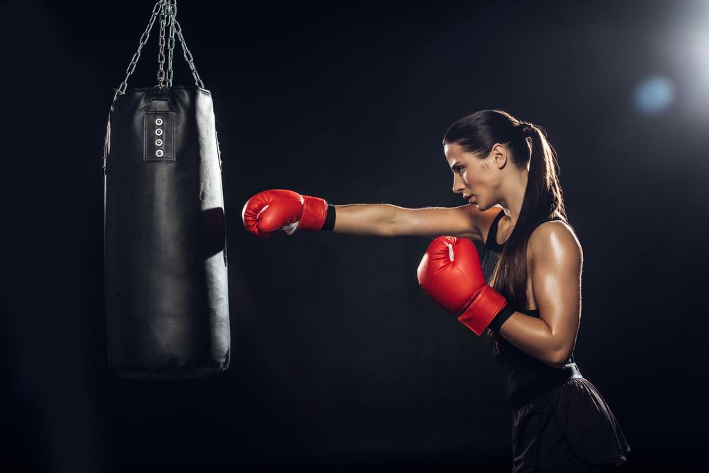 Boční pohled na ženský boxer v červených boxerských rukavicích s děrovací brašnu - Fotografie, Obrázek