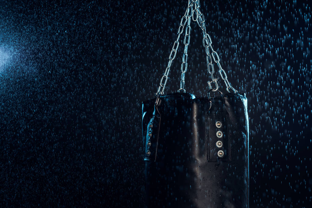 Bolso de perforación de cuero colgado en cadenas de acero bajo gotas de agua en negro
 - Foto, Imagen