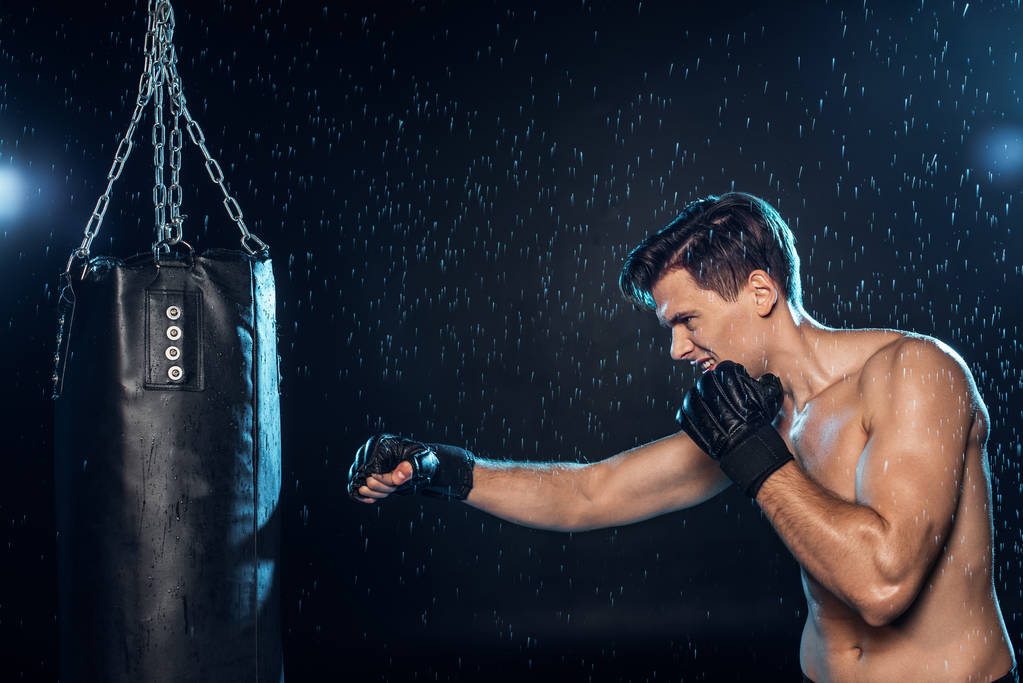 Boxer training met bokszak onder water druppels op zwart - Foto, afbeelding