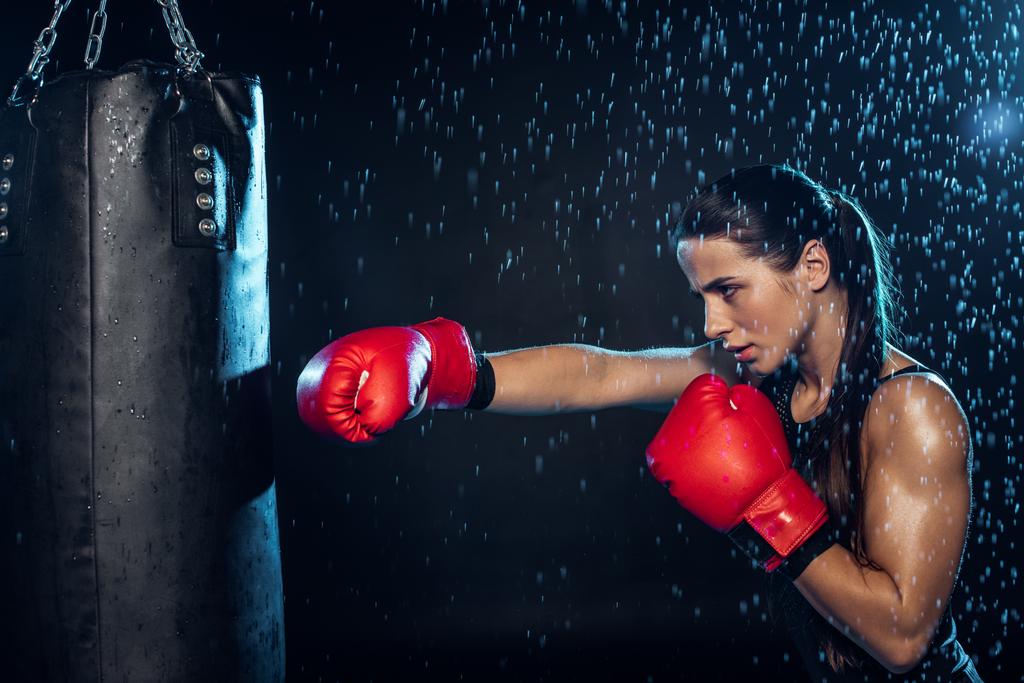 Nachdenklicher Boxer in roten Boxhandschuhen trainiert unter Wassertropfen auf schwarz - Foto, Bild