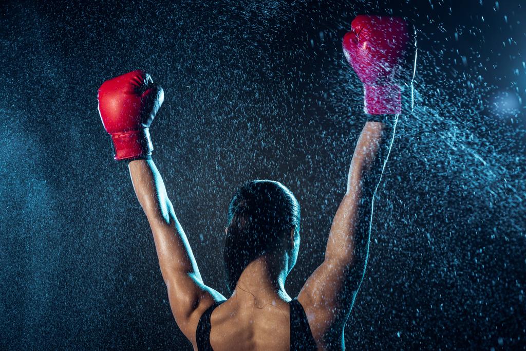 Вид сзади боксера в красных боксёрских перчатках, показывающий жест "да" на чёрном
 - Фото, изображение