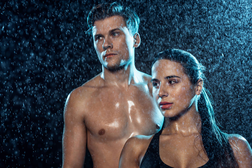 Sporty uomo e donna in piedi sotto gocce d'acqua e guardando altrove
 - Foto, immagini