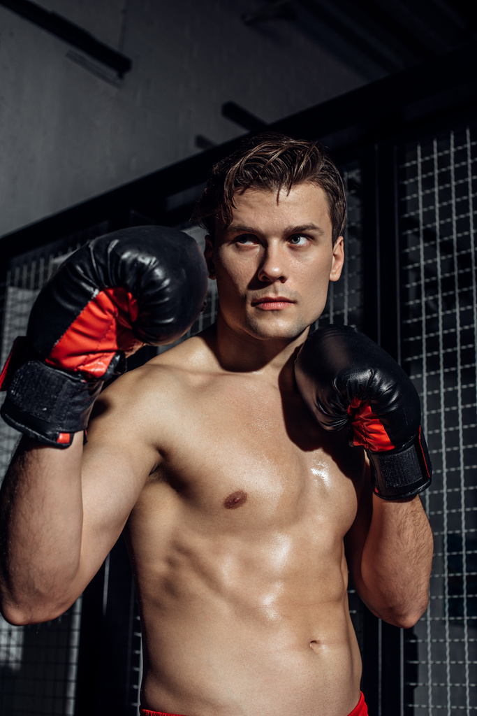 Pensive boxer em luvas de boxe preto com as mãos para cima olhando para longe
 - Foto, Imagem