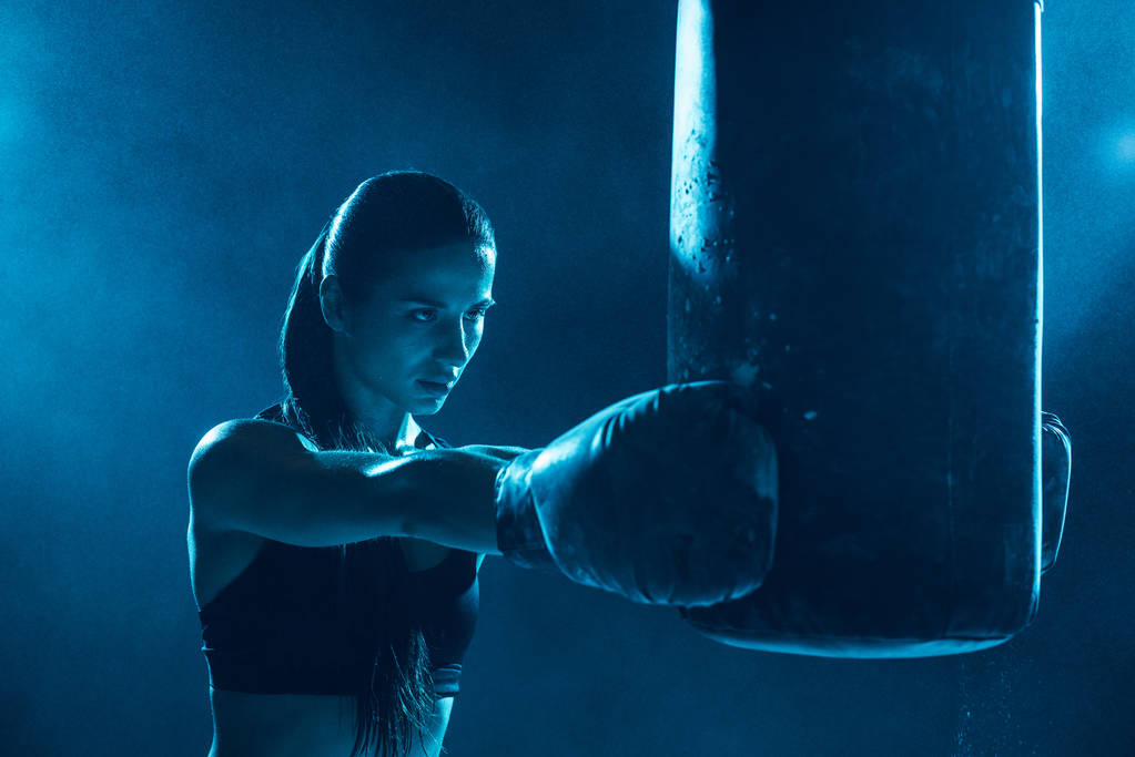 Female boxer in boxing gloves training with punching bag - Photo, Image