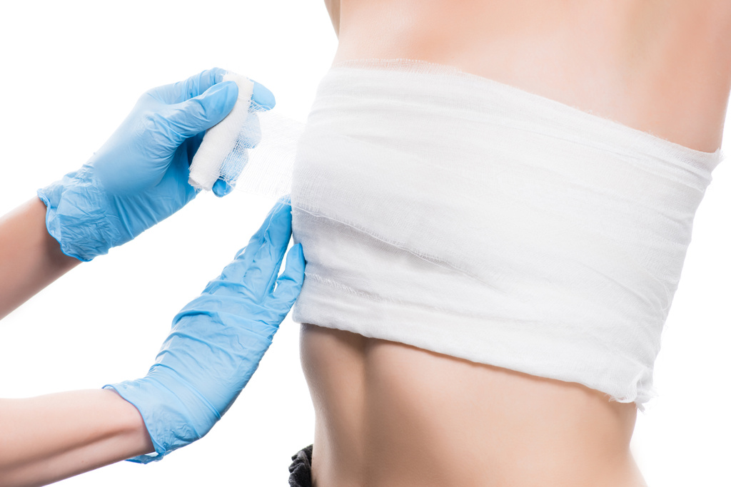 cropped view of plastic surgeon in blue latex gloves bandaging breast of woman isolated on white  - Photo, Image