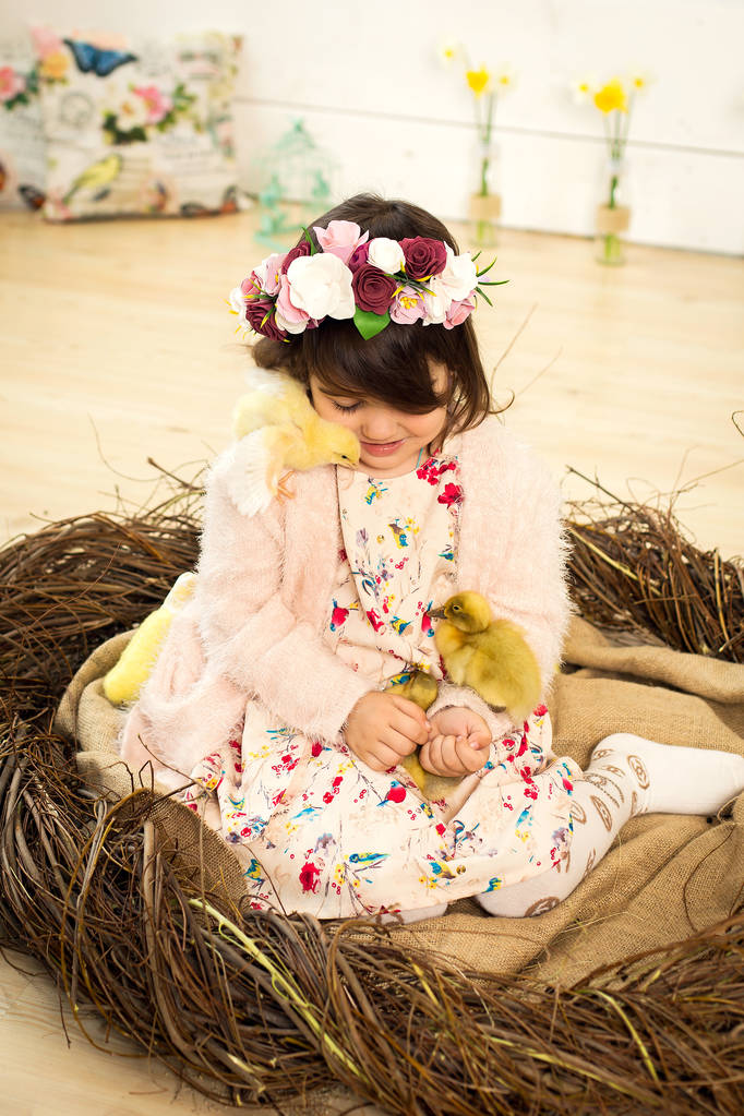 щаслива маленька дівчинка в сукні сидить в гнізді і тримає милий пух
 - Фото, зображення