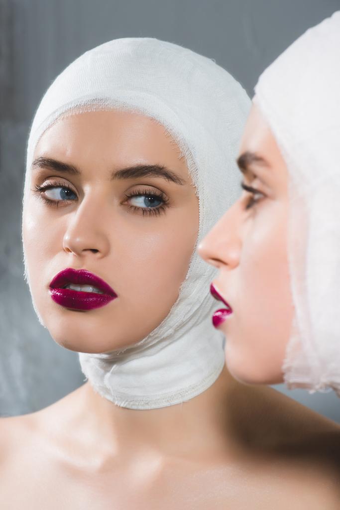 зеркальное отражение молодой красивой женщины с перевязанной головой на серой
  - Фото, изображение