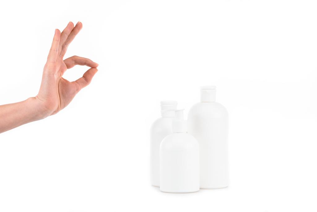 Bijgesneden weergave van meisje met cosmetische flessen resultaat oke teken geïsoleerd op wit - Foto, afbeelding