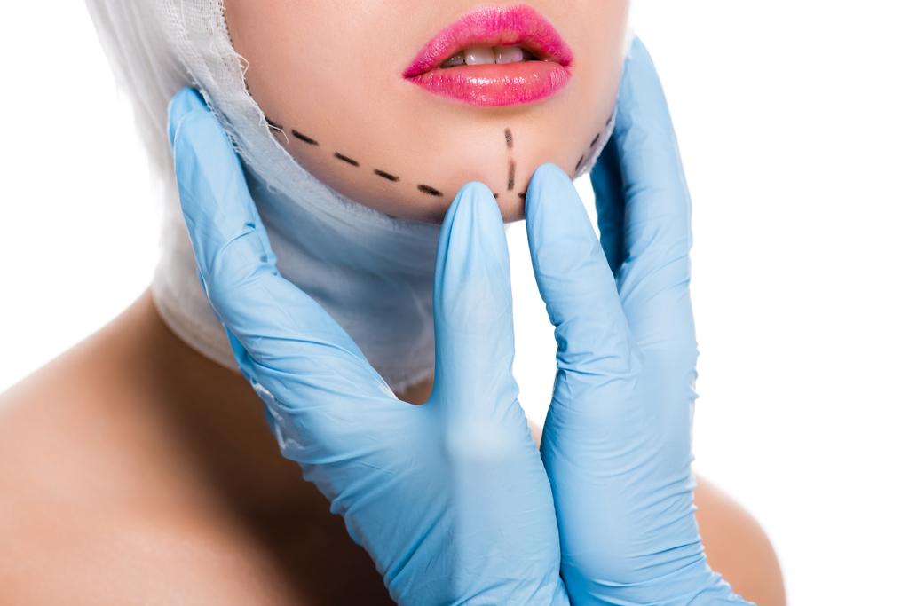 cropped view of plastic surgeon in blue latex gloves touching woman with marks on face isolated on white  - Photo, Image