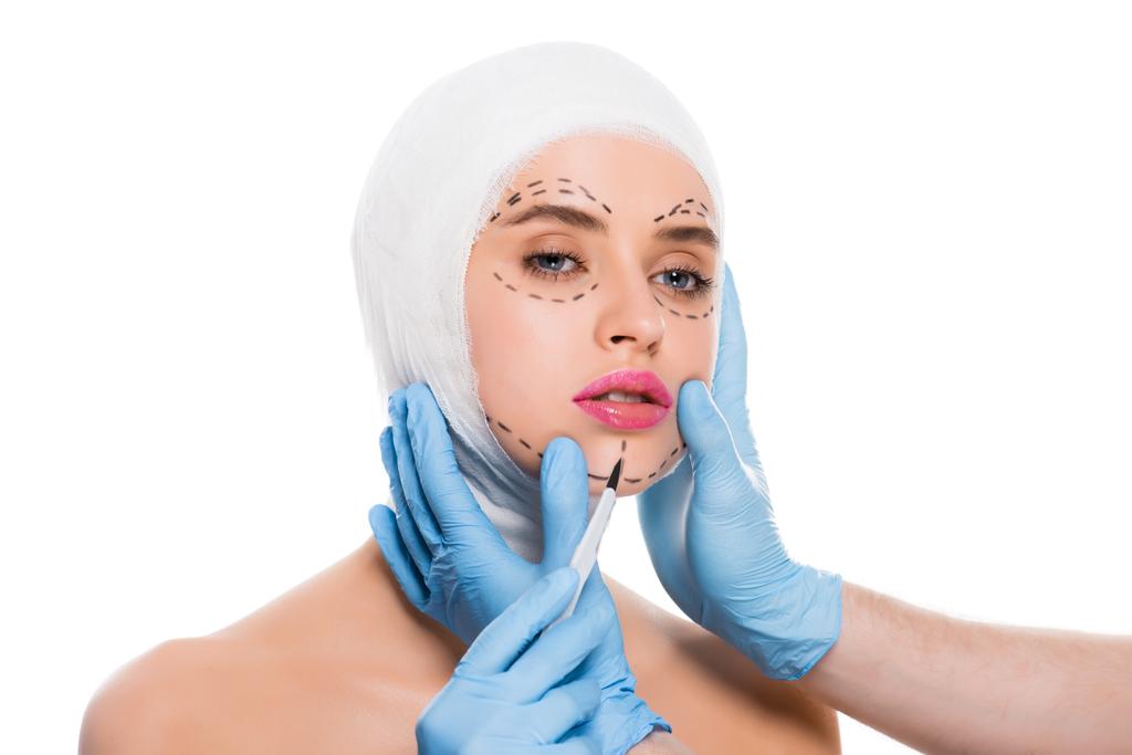 Ausgeschnittene Ansicht des plastischen Chirurgen in blauen Latex-Handschuhen mit Skalpell im Gesicht der Frau mit isolierten weißen Flecken  - Foto, Bild